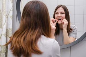 Woman placing clear aligners on her teeth in the mirror.