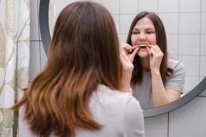Woman placing clear aligners on her teeth in the mirror.